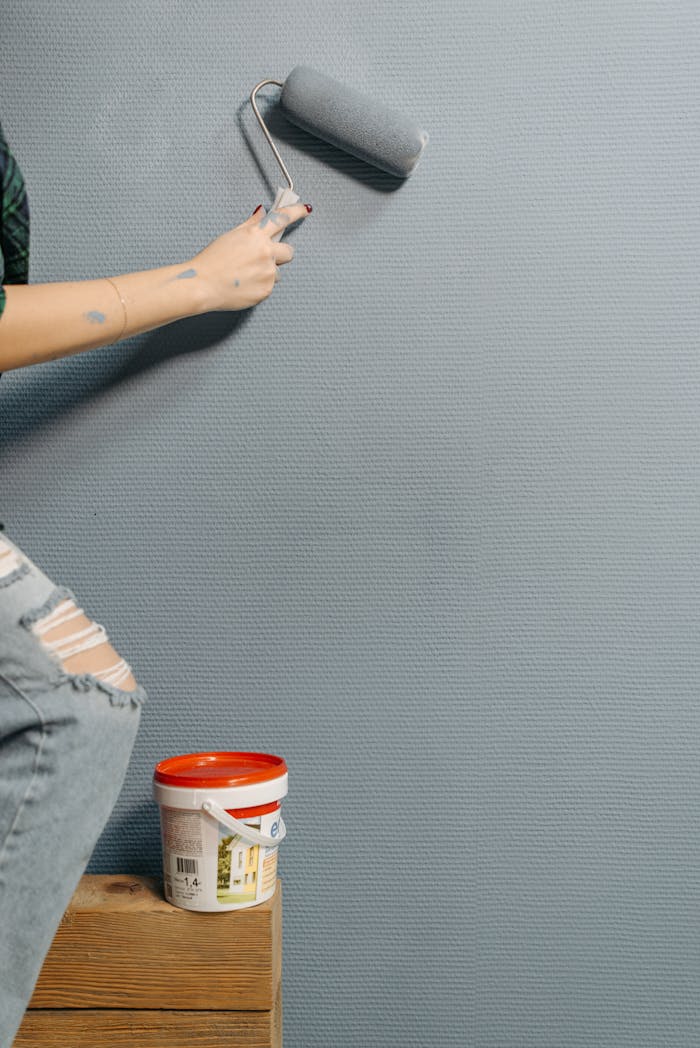 An adult painting a textured wall with a paint roller during home renovation.